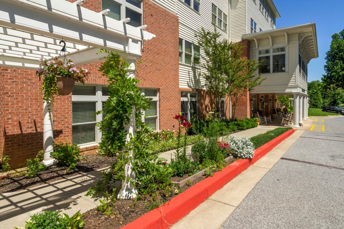 A well-maintained garden area outside a brick and white building, featuring lush plants and a paved pathway.