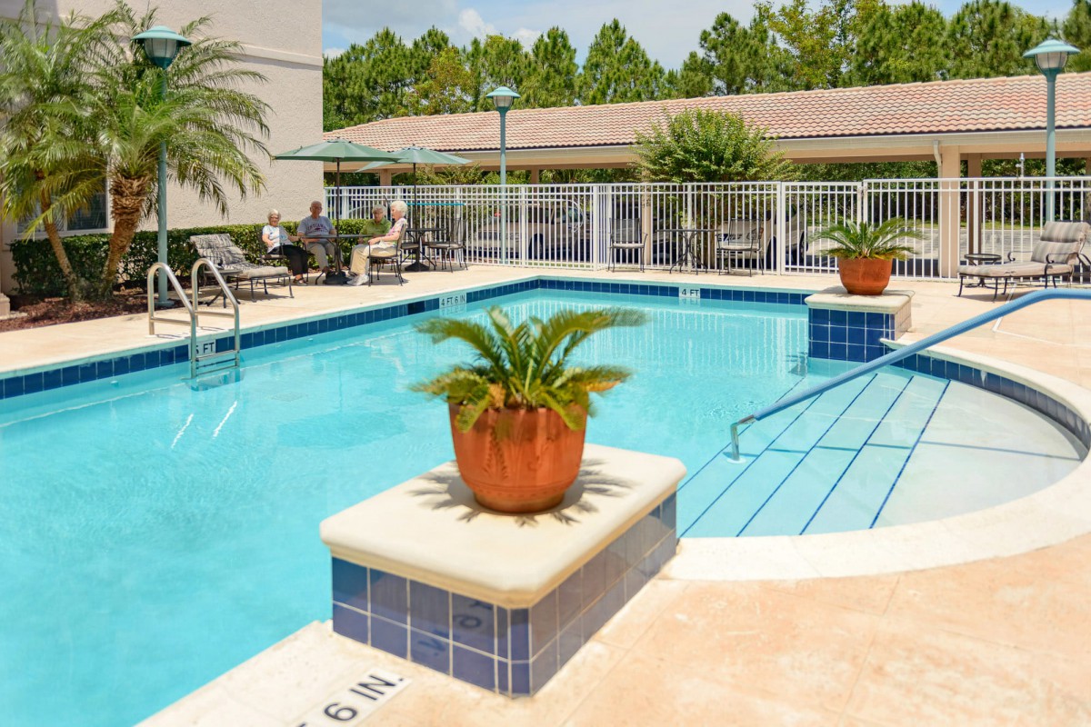 A tranquil outdoor swimming pool surrounded by lush greenery and palm plants, perfect for relaxation on a sunny day.