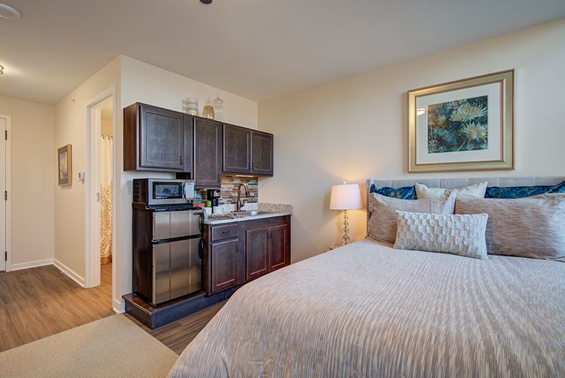 A cozy apartment bedroom with a kitchenette, featuring modern furniture and amenities.