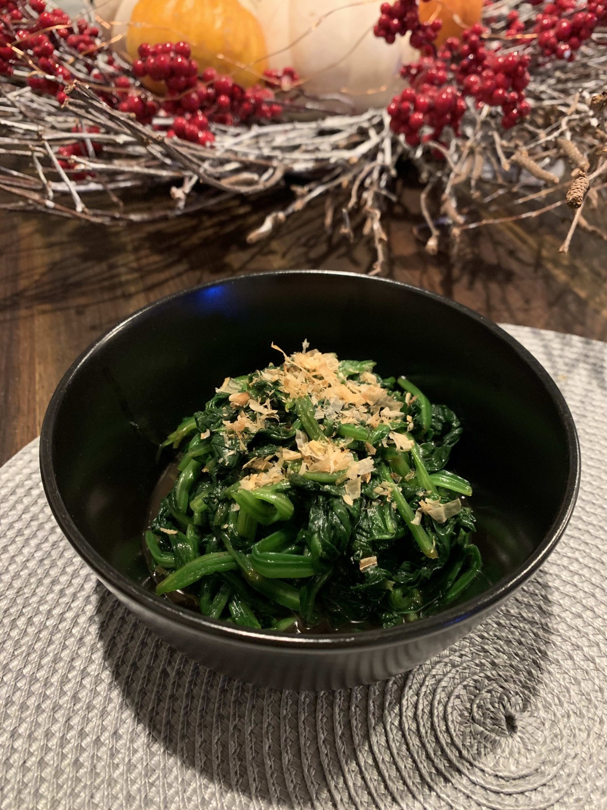 A bowl of fresh spinach garnished with a topping, placed on a textured mat.