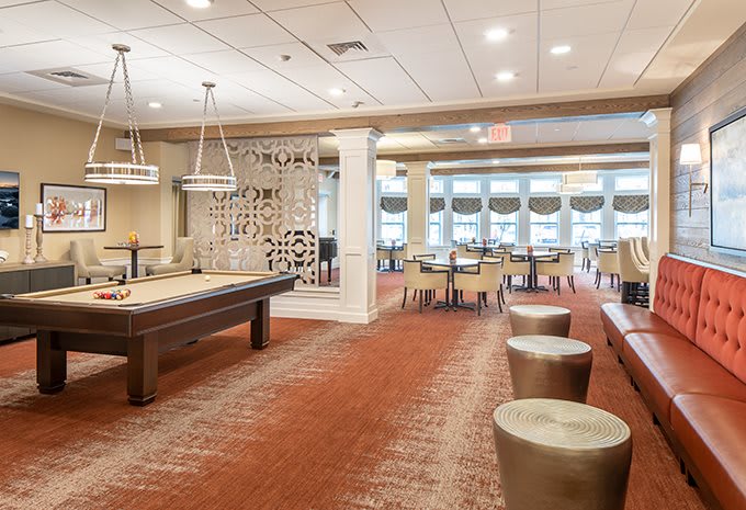 A modern recreation room featuring a shuffleboard table and ample seating.