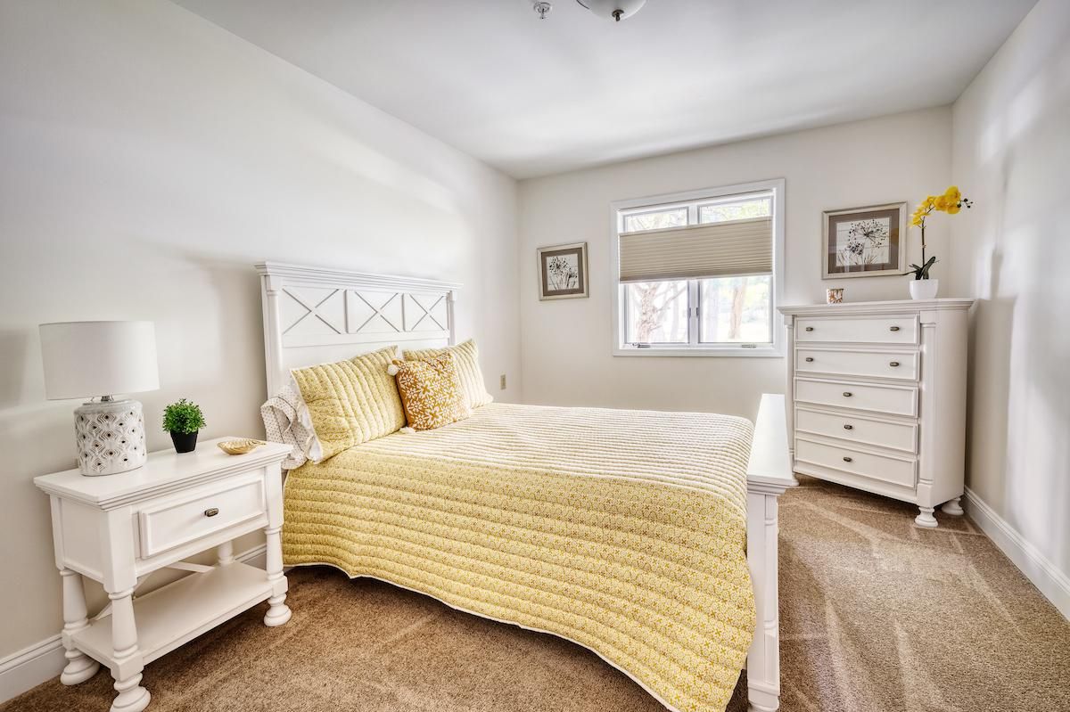 A cozy bedroom featuring a yellow bedspread, white furniture, and soft lighting.