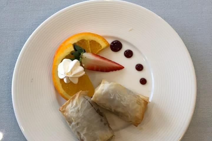 A beautifully presented dessert featuring pastry rolls with fresh fruit garnishes including orange slices, a strawberry, and a dollop of cream.