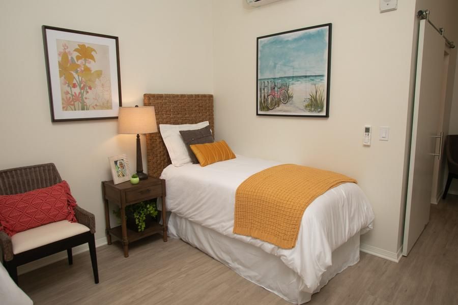 A cozy bedroom with a single bed adorned with orange accents, complemented by tasteful artwork and a warm lamp.