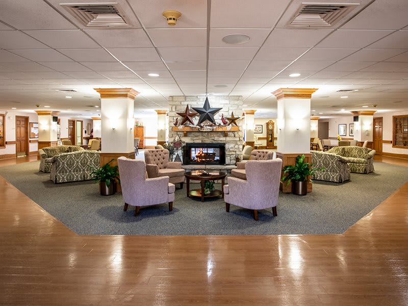 A cozy lobby interior featuring a seating area with armchairs around a fireplace, complemented by warm lighting and decorative elements.
