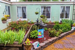 A charming garden with a central fountain, surrounded by greenery and decorative elements in front of a house.