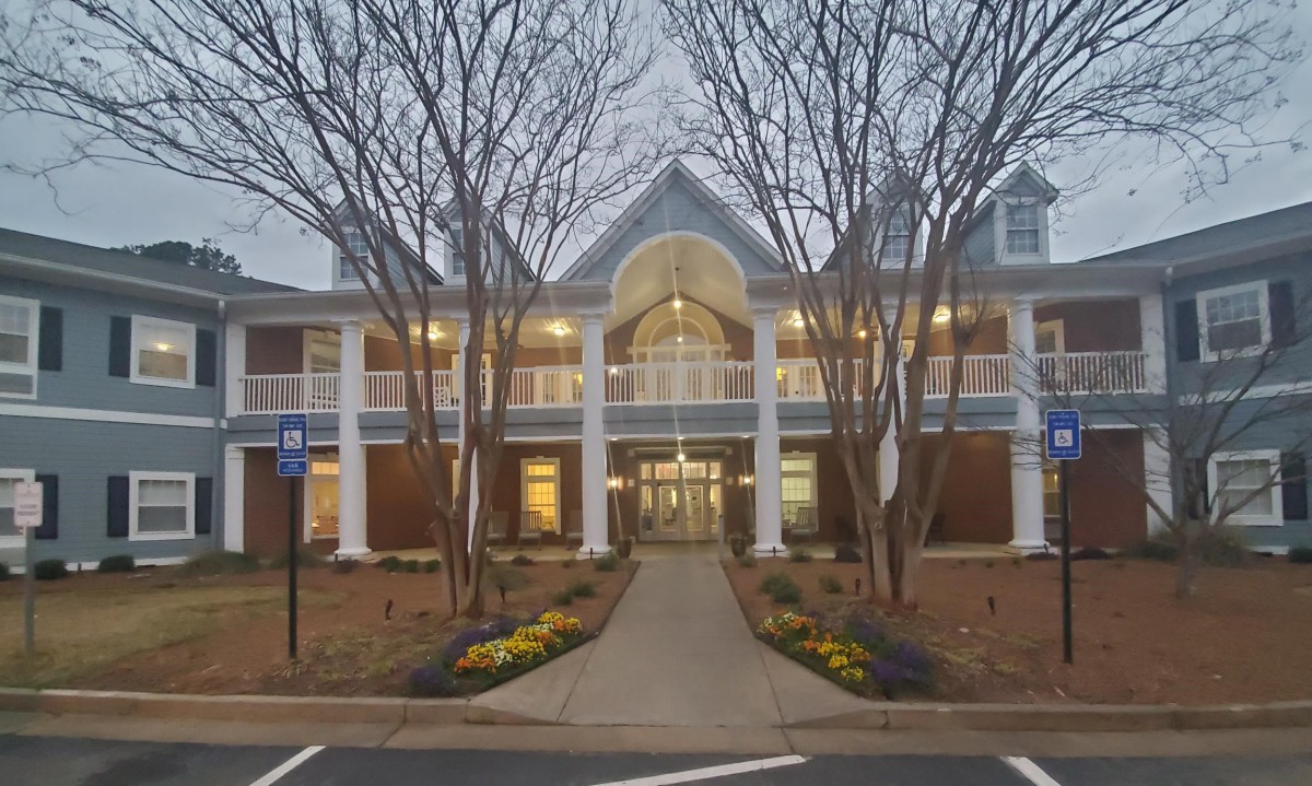 A symmetrical building with large windows and an inviting entrance, flanked by trees and illuminated by glowing lights.