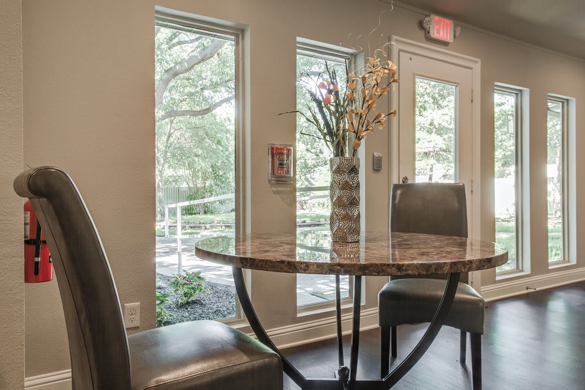 A cozy dining area with a round table and chairs, illuminated by natural light from large windows.