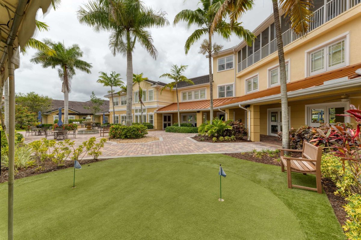 A landscaped outdoor area with palm trees and a patio in front of a multi-story building.