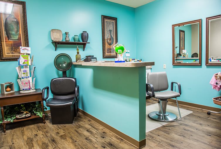A cozy hair salon with turquoise walls, featuring styling chairs, a mirror, and a hair dryer set against a wooden floor.