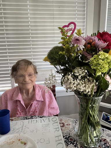 An elderly woman enjoying the company of a beautiful bouquet of flowers at her table.