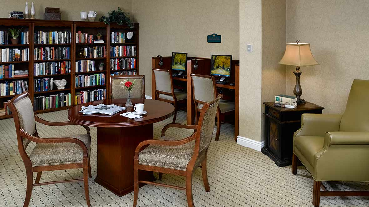 A cozy library corner with a round table, chairs, bookshelves, and computer stations.