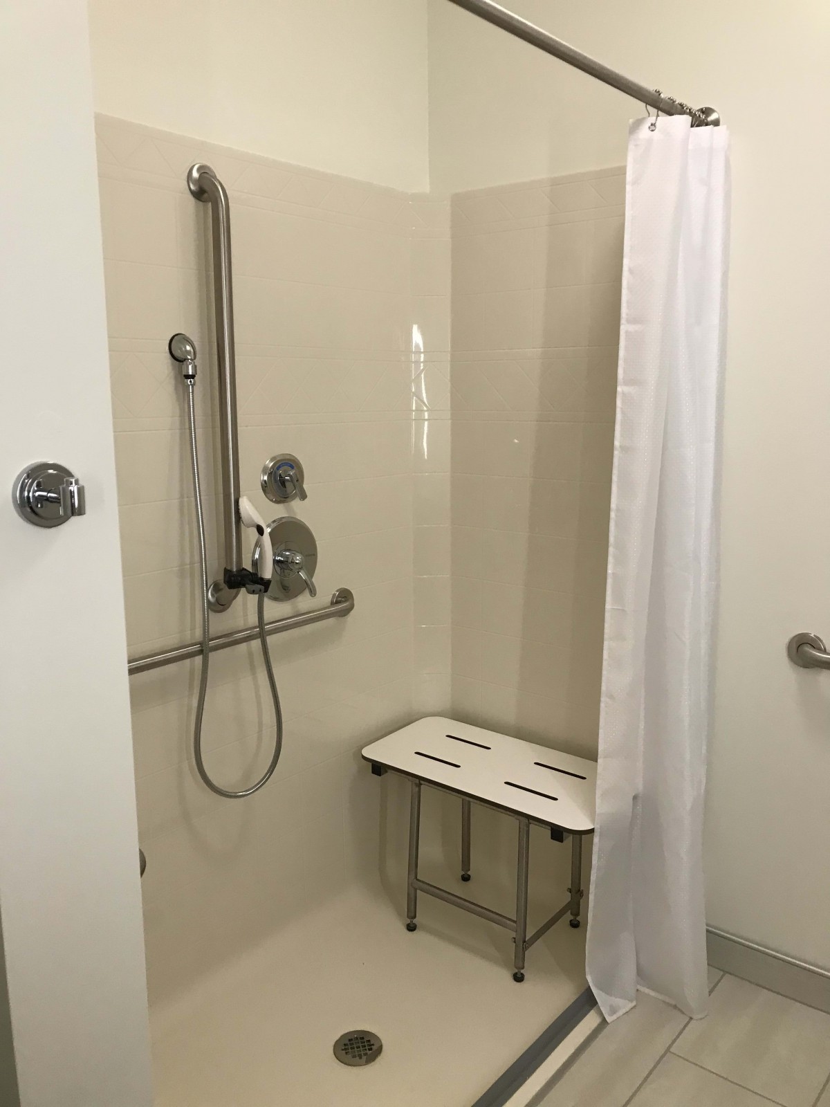 An accessible bathroom shower with a chair and safety grab bars.