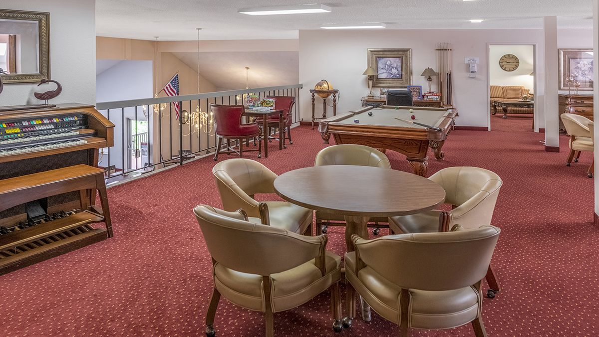 A cozy indoor game room featuring a billiards table and a seating area with chairs and tables.