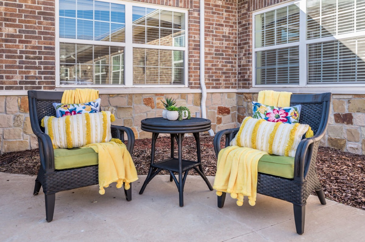 A cozy outdoor patio setting featuring two cushioned chairs with decorative pillows and blankets, alongside a small table with a plant.