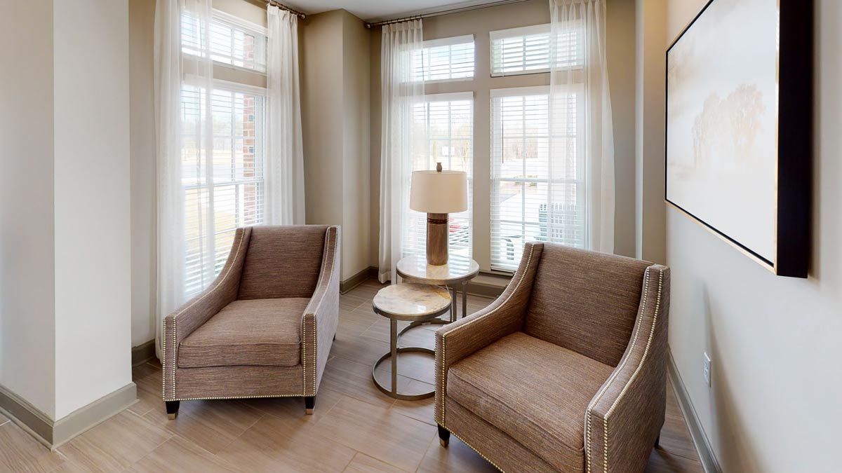 A cozy living room corner with two armchairs, a small table, and a lamp by the window.