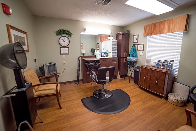 Interior of a barbershop with a central chair facing a mirror and various furniture pieces.