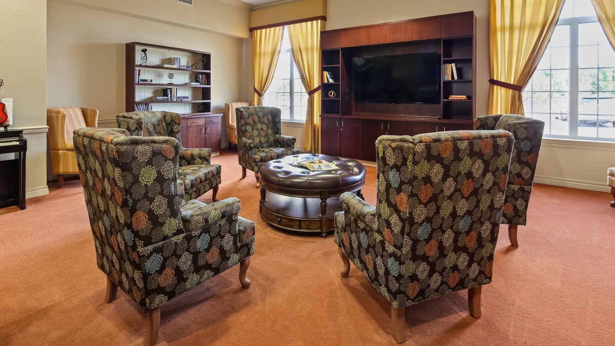 A cozy living room with patterned armchairs, a central coffee table, and built-in bookshelves framing a large television.