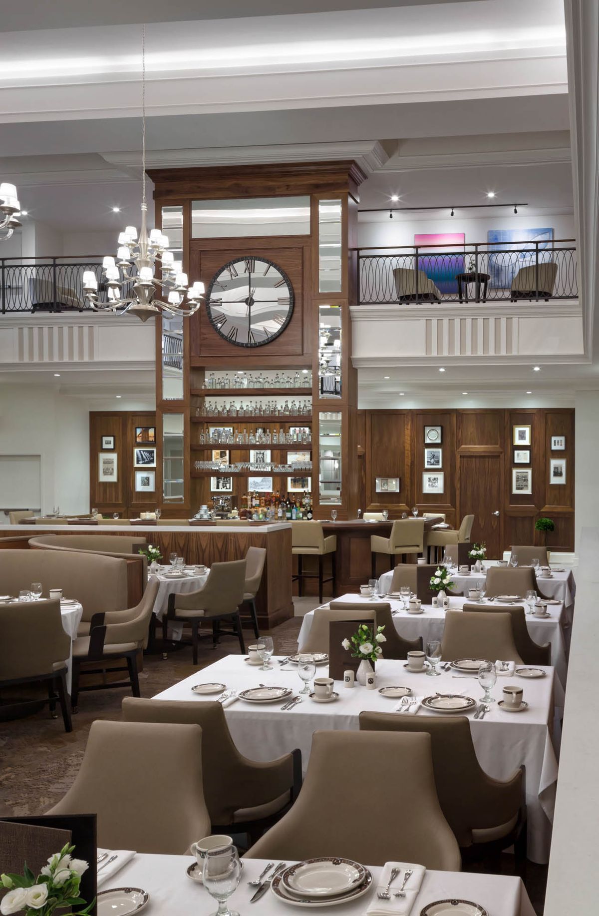 A sophisticated restaurant interior featuring a large clock, elegant chandelier, and neatly arranged dining tables.