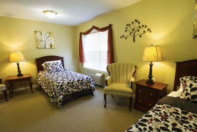 A cozy bedroom with two single beds, a lamp, and a decorative chair.