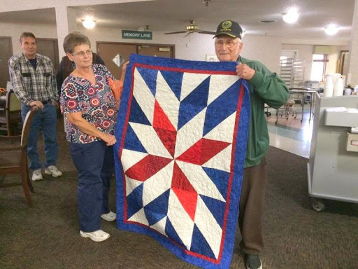 Two individuals proudly display a beautifully crafted quilt featuring a vibrant star design in red, white, and blue.