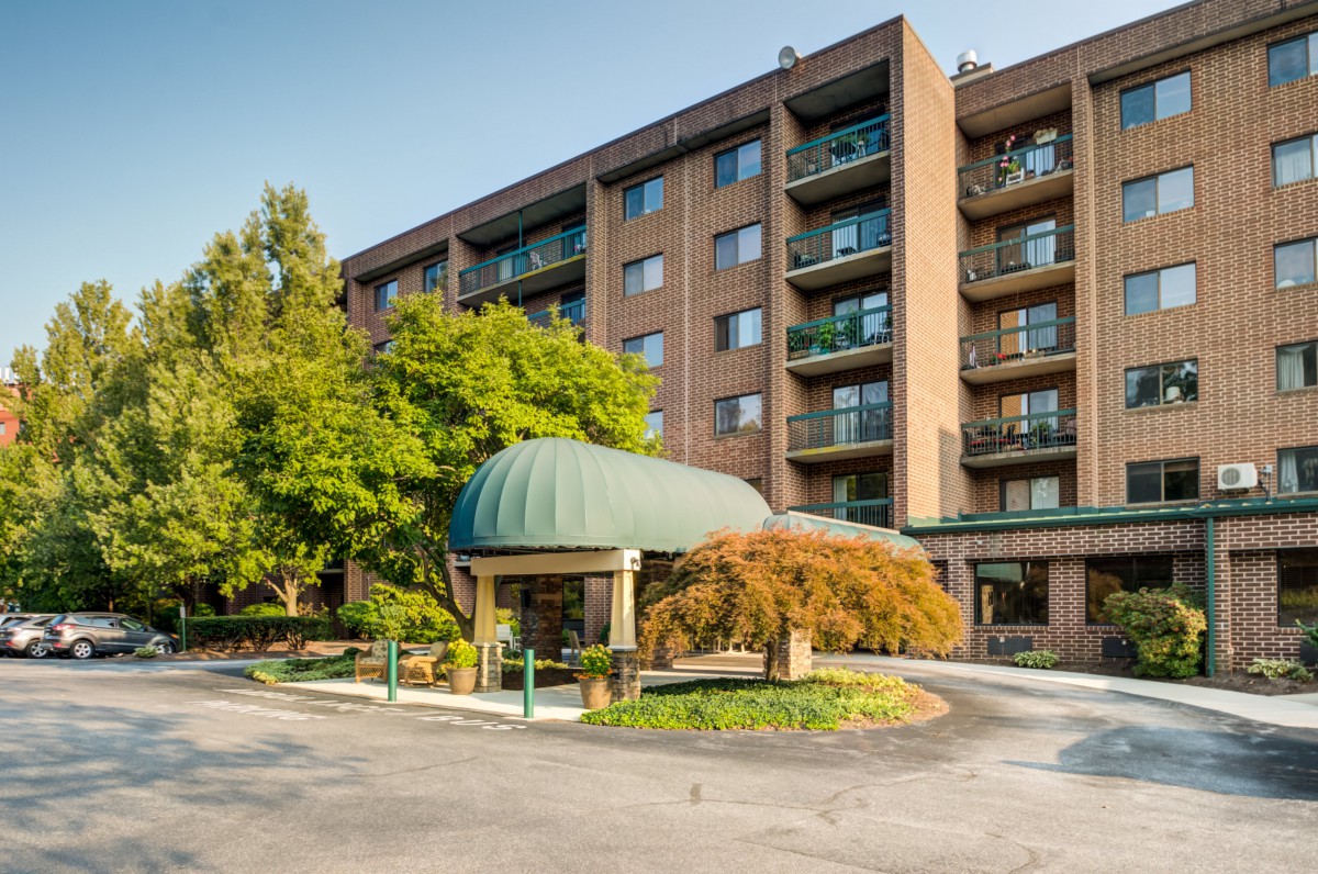 A multi-story hotel with a green canopy entrance surrounded by trees.