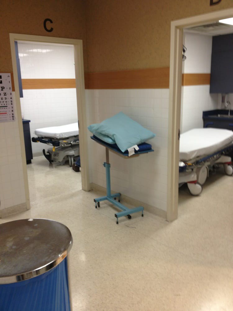A hospital hallway with empty medical beds and a small table with linens.