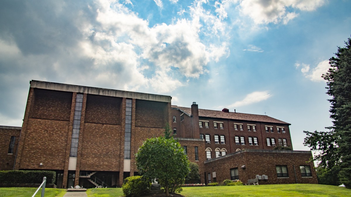 A brick building with a cloudy sky and lush greenery in the foreground.