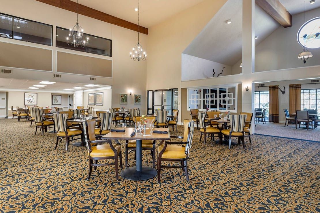A spacious dining area with elegant decor, featuring tables and chairs under chandeliers.