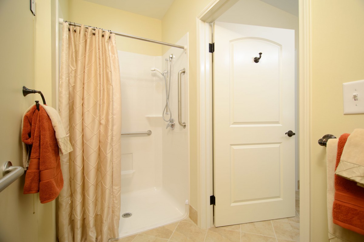 A bathroom featuring a walk-in shower with grab bars, a curtain, and a closed door.
