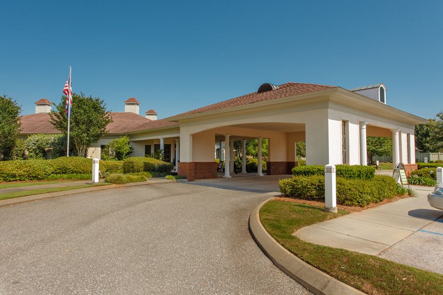 A sunny day view of a building entrance with a driveway and surrounding greenery.