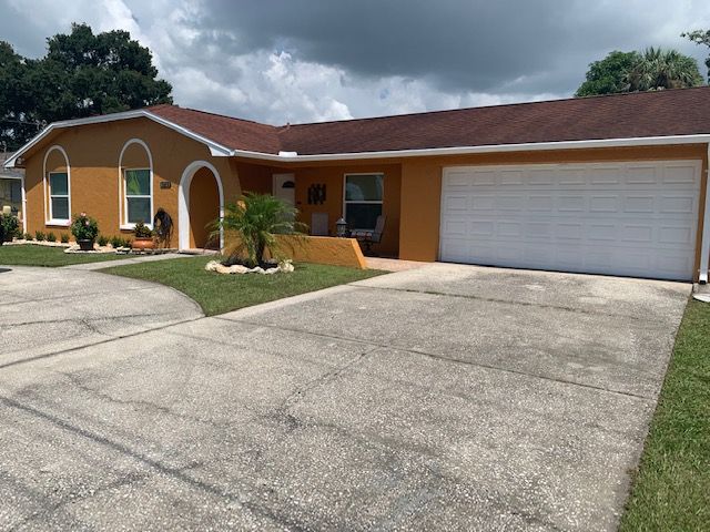 A single-story house with a garage and driveway under a cloudy sky.