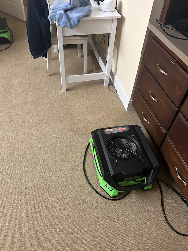 A carpet dryer positioned on the floor near some furniture.