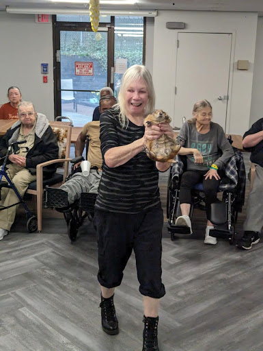 An engaging moment at a community center where an elderly woman joyfully holds a small animal while others look on with smiles.