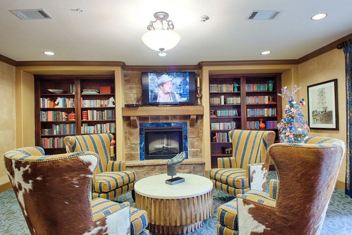 A cozy library setting with armchairs in front of a fireplace, surrounded by bookshelves and a mounted television.