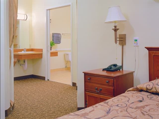 A hotel room featuring a bed, nightstand with a lamp, and an adjacent bathroom.