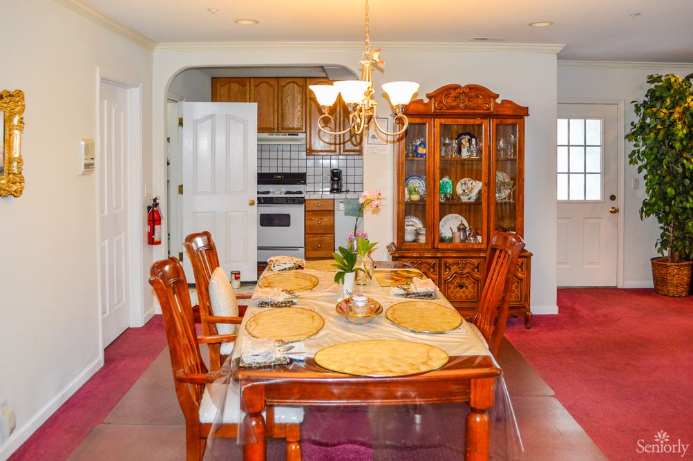 Elegant dining room with a set dining table, chandelier, and view into the kitchen.