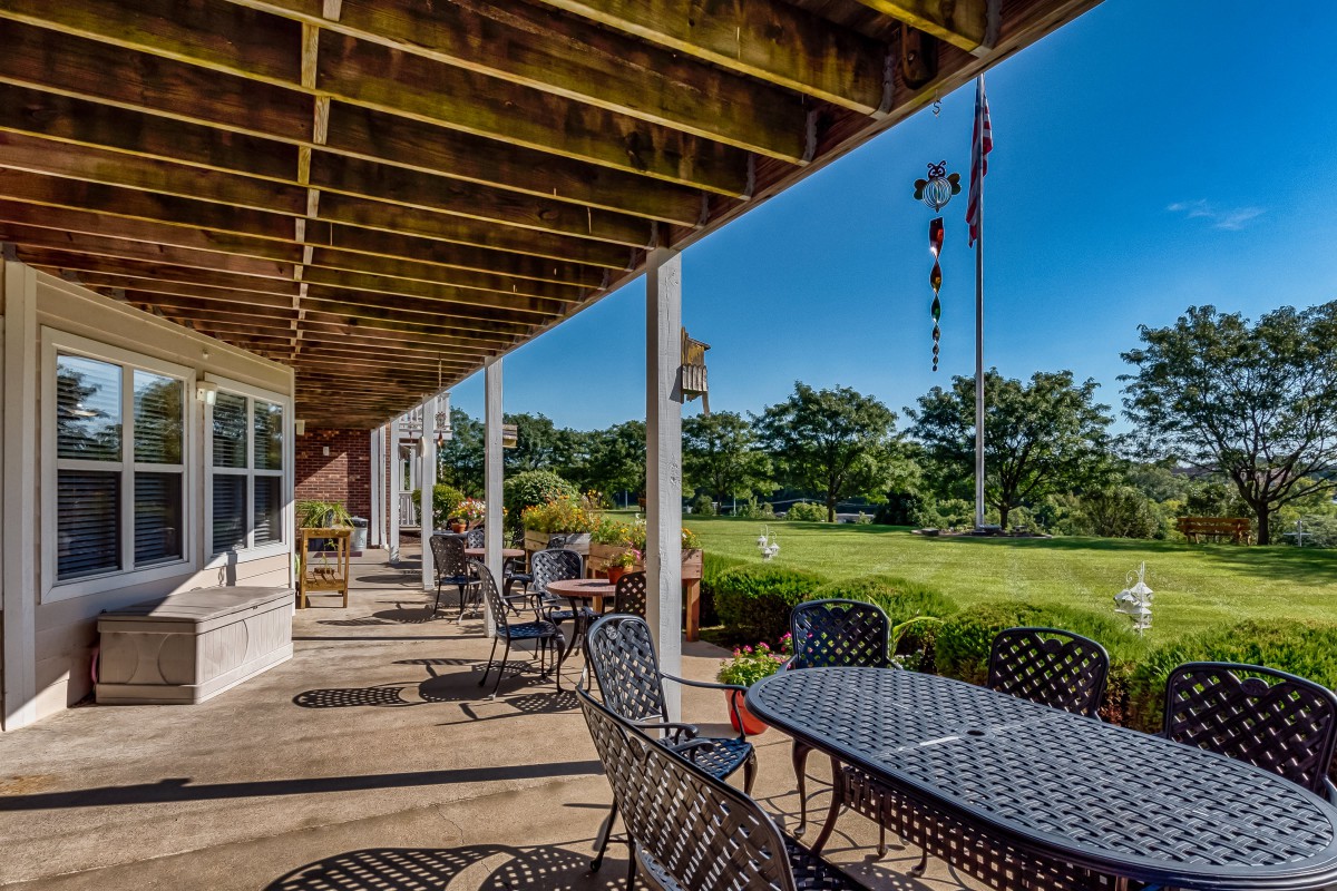 A spacious patio with metal tables and chairs overlooks a lush garden on a sunny day.