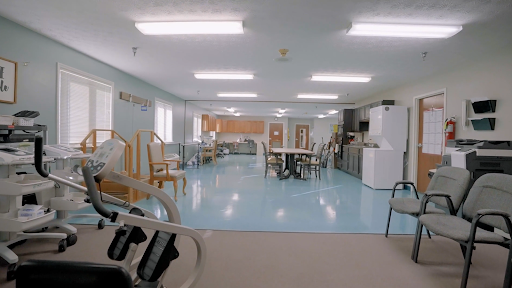 A spacious common area with seating and a kitchen in the background, featuring blue flooring and bright overhead lights.