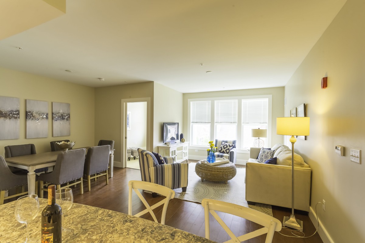 A spacious and well-lit living room with an open dining area, featuring modern furniture and large windows.