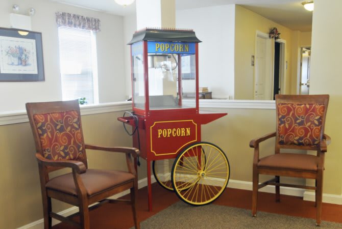 A vintage popcorn machine situated between two wooden chairs in a cozy interior setting.