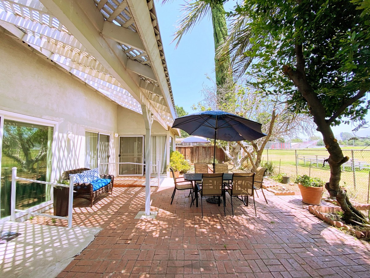 A sunny outdoor patio with garden furniture and an umbrella, surrounded by lush trees.
