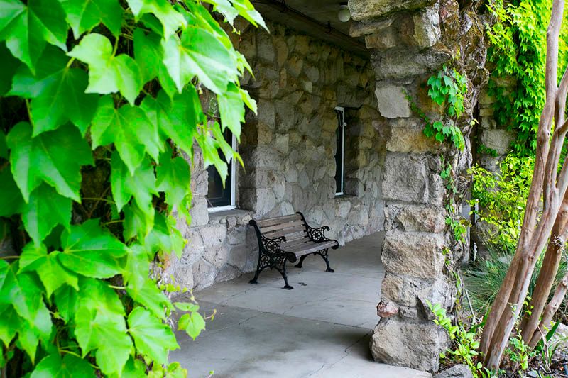 A stone porch adorned with ivy, featuring a bench against the wall.