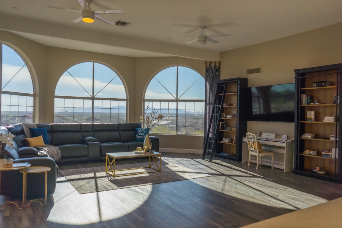 A spacious living room with large arched windows allowing ample natural light, featuring a comfortable sofa, elegant coffee table, wall-mounted TV, and a neatly organized bookshelf.