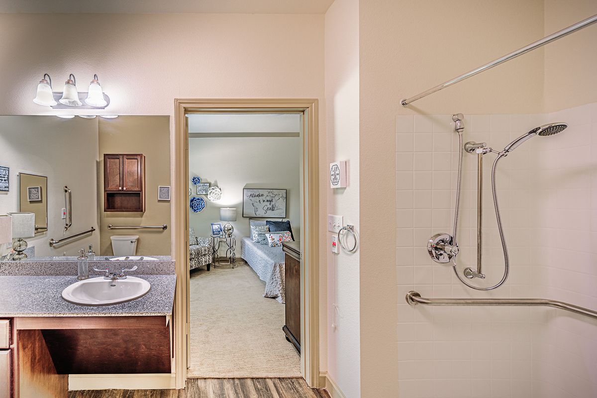 An accessible hotel bathroom with a view into the bedroom, featuring a shower and sink.