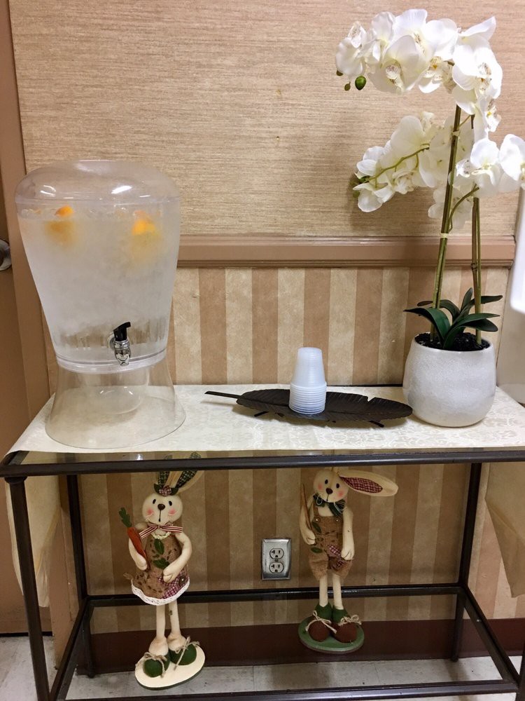 A decorative table with a lemon-infused water dispenser, orchids, and two hanging dolls.