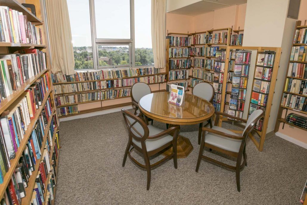 A cozy library corner with a round table and chairs surrounded by shelves of books.