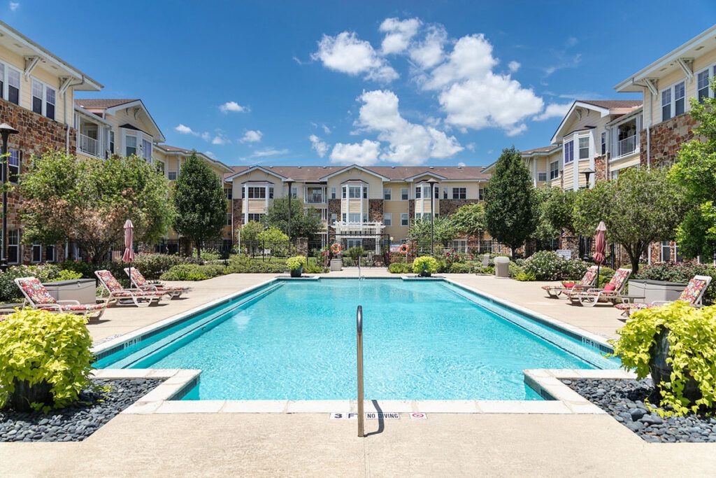 A sunny day view of a swimming pool surrounded by an apartment complex and landscaped gardens.