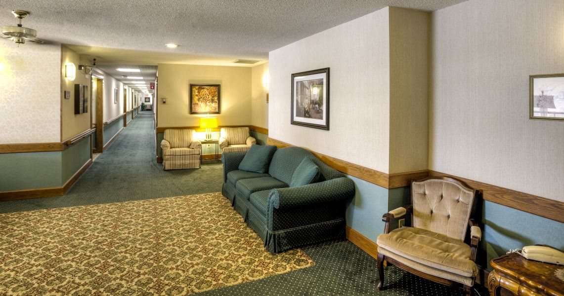 A cozy hotel lobby featuring a sofa, carpeted floors, and framed artwork on the walls.
