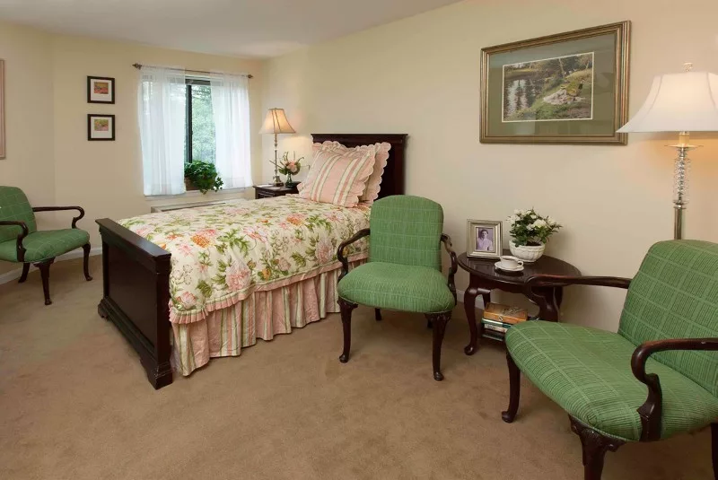 A cozy bedroom with floral bedspread, green armchairs, and soft lighting.